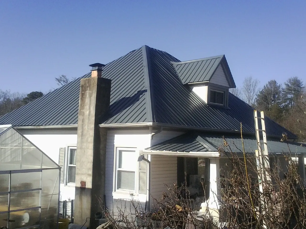 Dark blue standing seam metal roof on a white farmhouse with dormer — Slate & Tile Roof Repair by Roofing Brothers in Wartburg