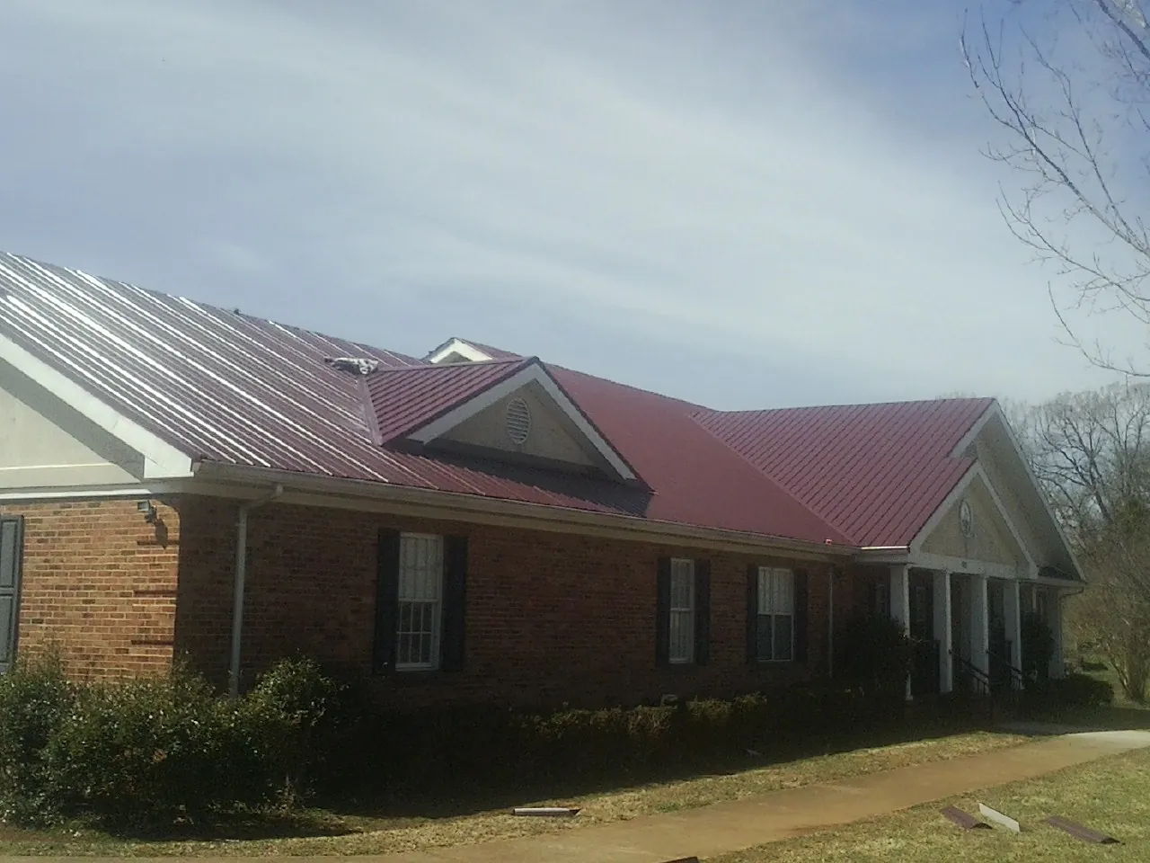 Red metal roof with gabled entries on a long brick building, from a Hail Damage Roof Repair job in Wartburg