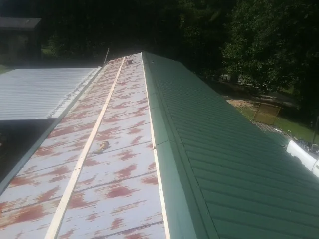 Old rusted panels beside newly installed green metal roofing — Wind Damage Roof Repair by Roofing Brothers in Wartburg