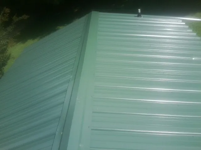 New green metal panels meeting at the ridge of a roof — Flat Roof Repair work by our crew in Wartburg