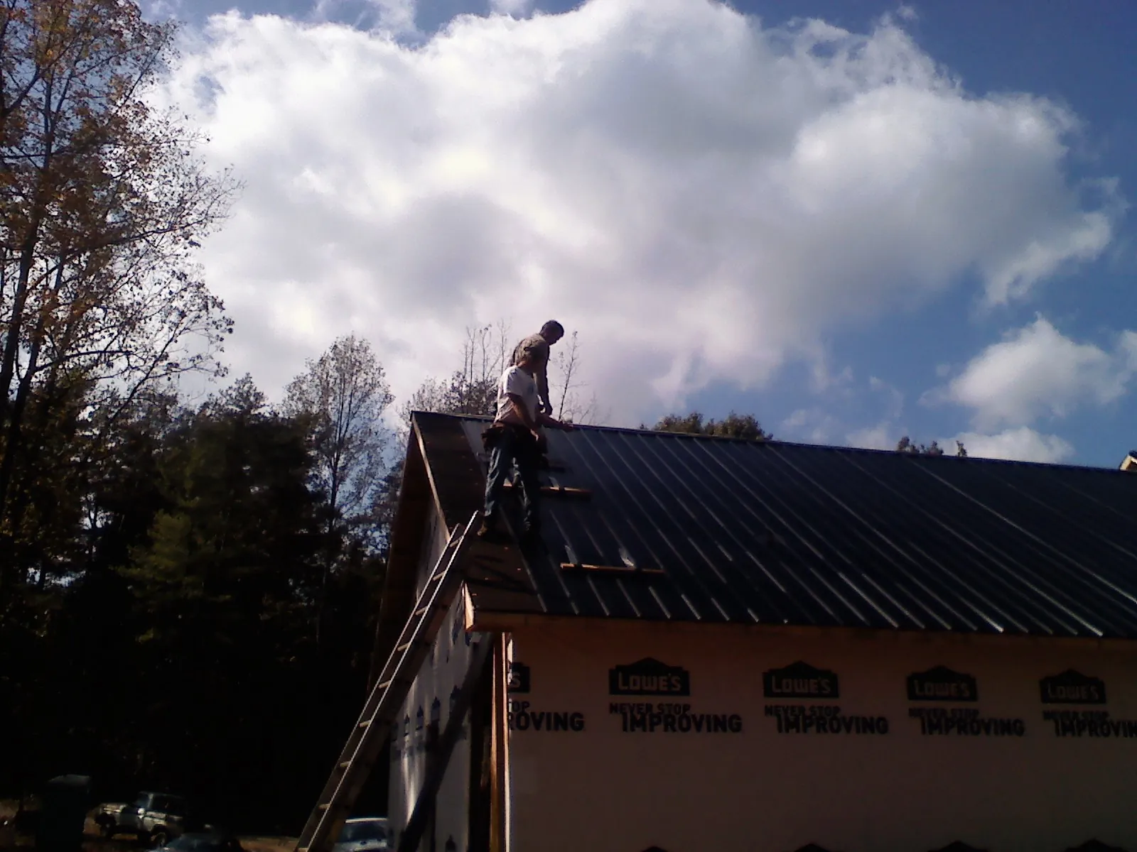 Roofer fastening dark metal panels high against a cloudy sky, from a Roof Inspection job in Wartburg