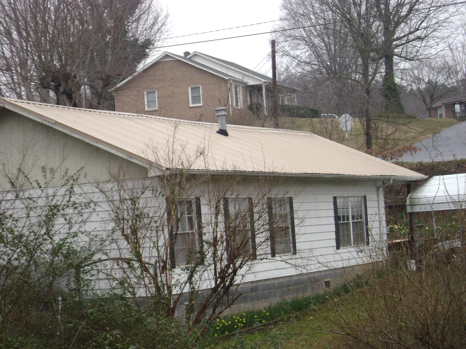 Tan metal roof on a white sided house set into a hillside — Commercial Roofing by Roofing Brothers in Wartburg
