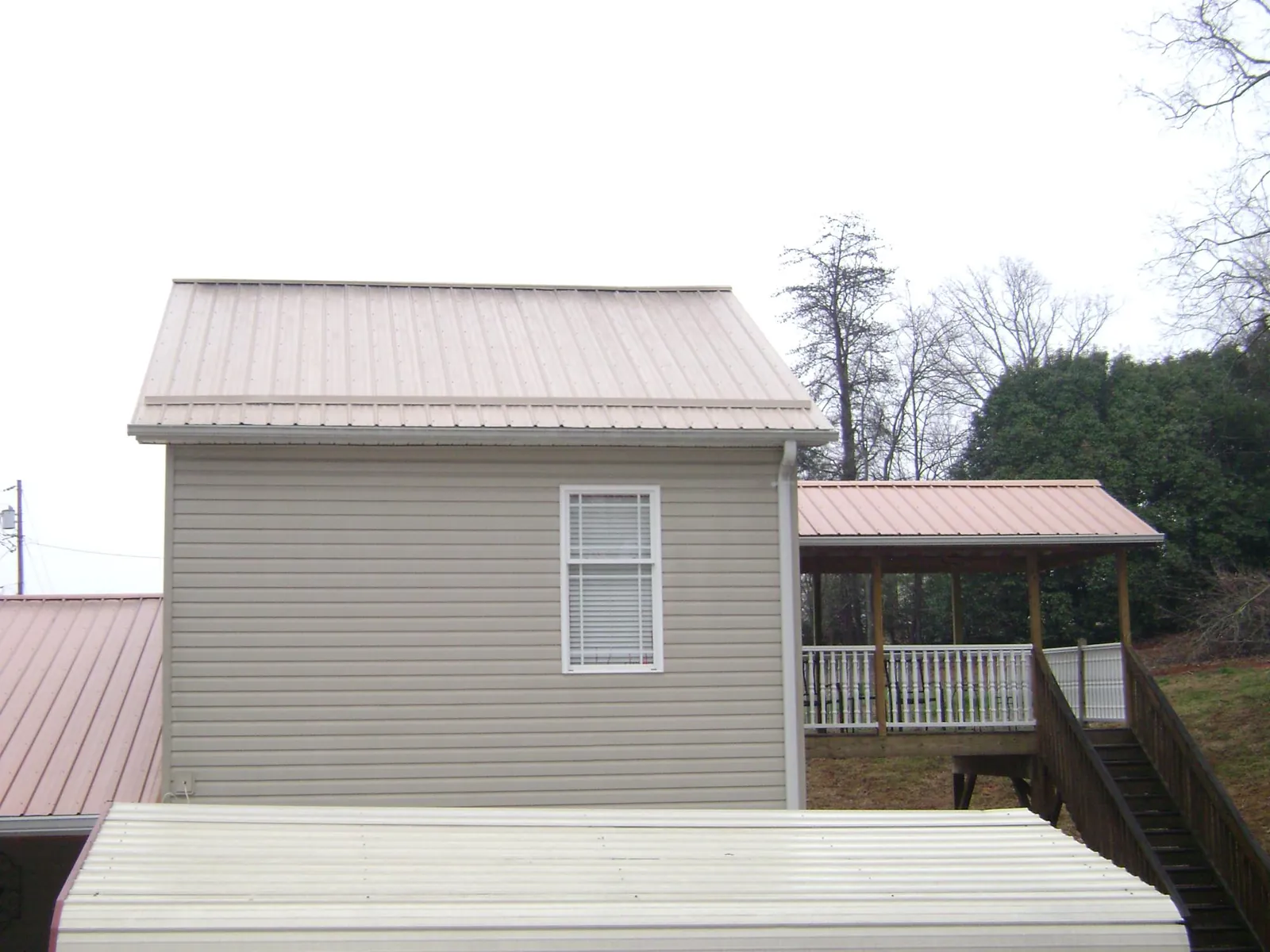 Tan metal roofs on a two story addition and attached porch, from a Roof Replacement job in Wartburg